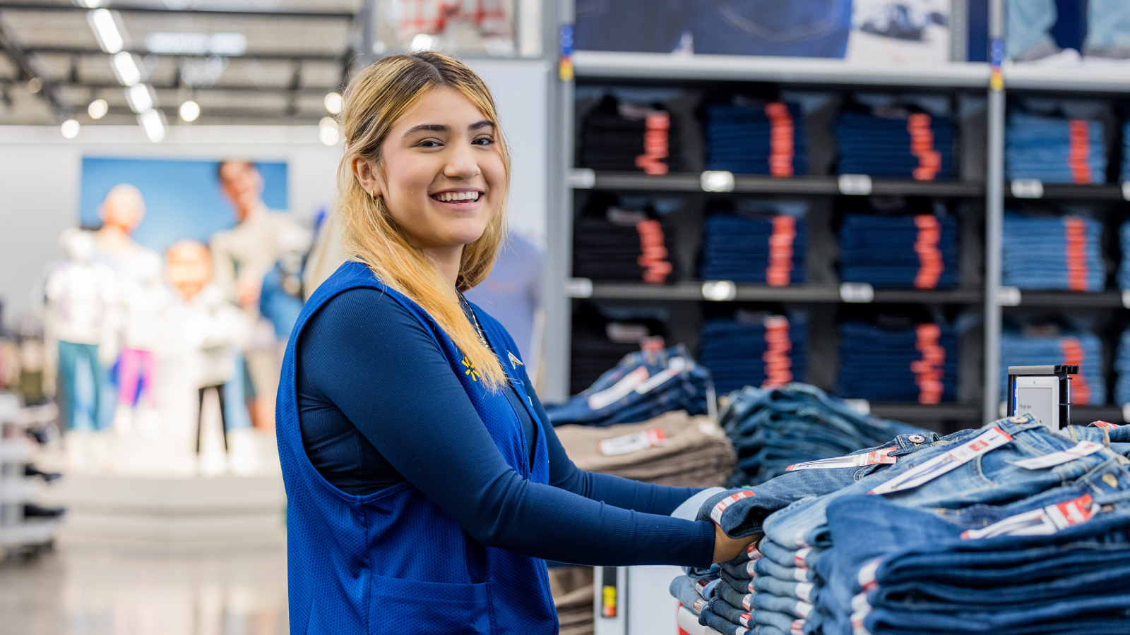 Associate folding denim and smiling at camera.