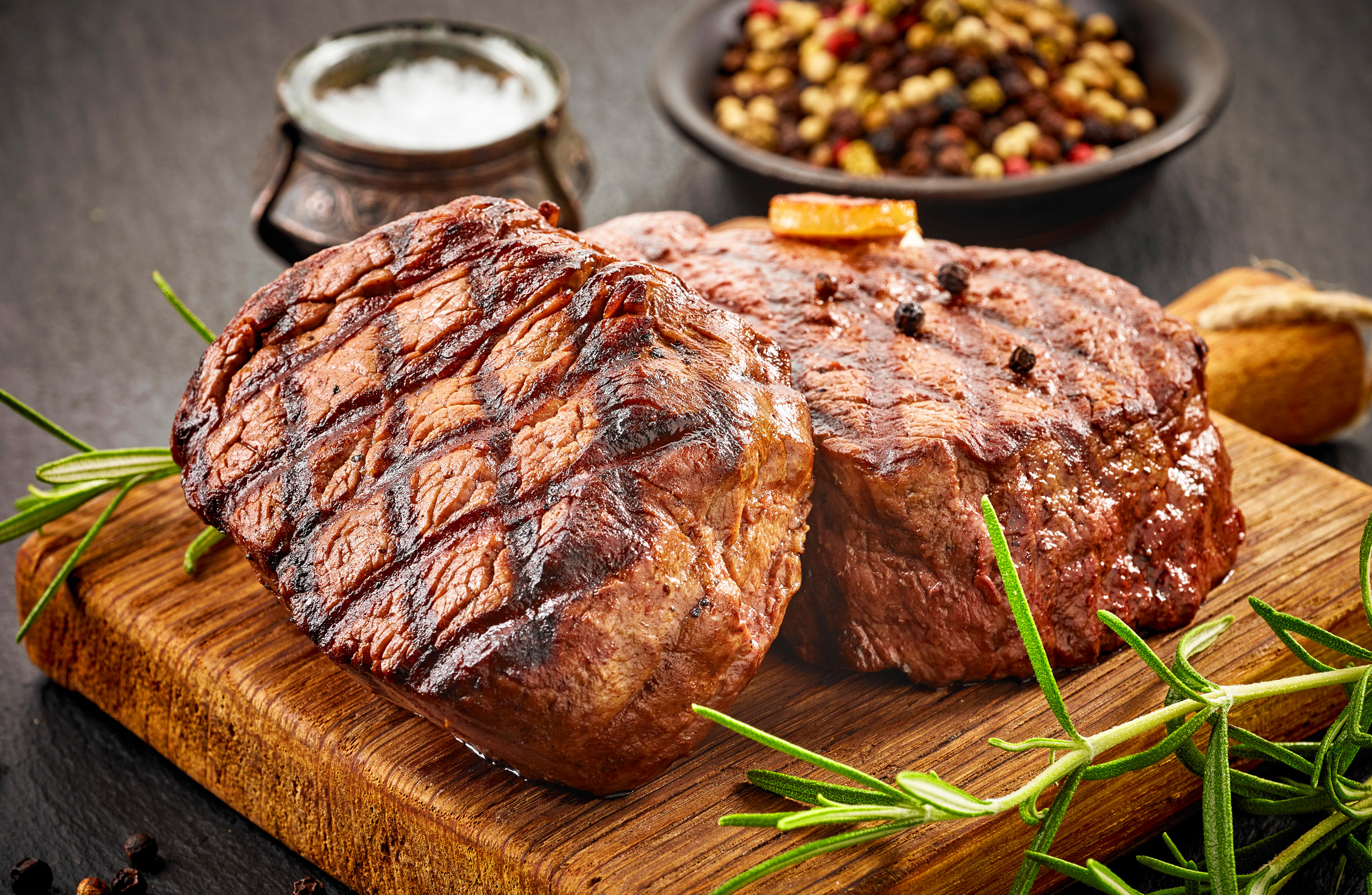 Steaks sitting on wood cutting board with course salt and peppercorn in the background