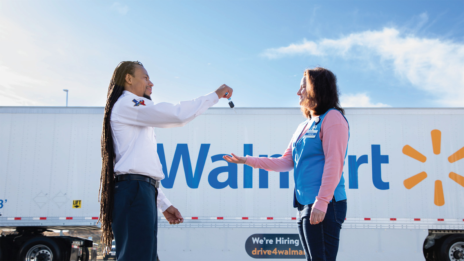 A Walmart truck driver drops keys into a Walmart associate's hands. A Walmart semi truck trailer can be seen in the background.