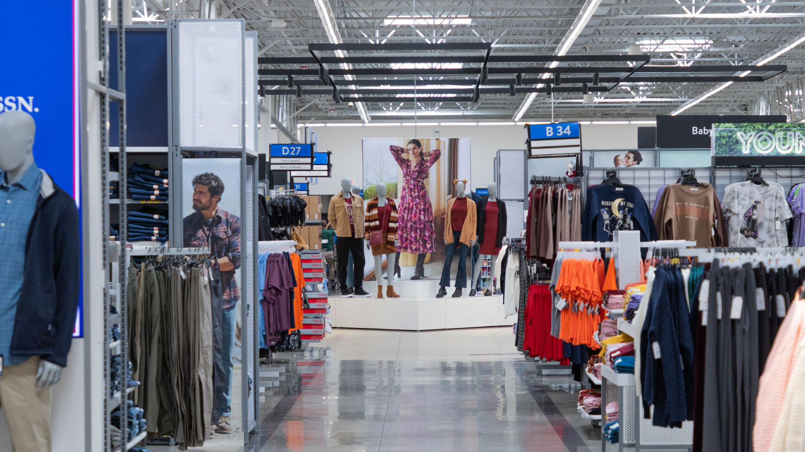 Wide shot looking down apparel department aisle with display of mannequins at end of aisle.