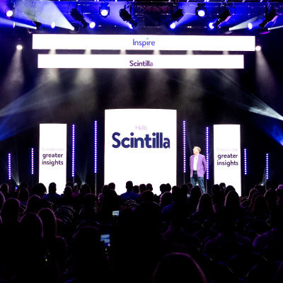 Wide angle view of stage at Inspire 2024 showing Scintilla logo. A large crowd in the foreground is a silhouette against the bright stage.