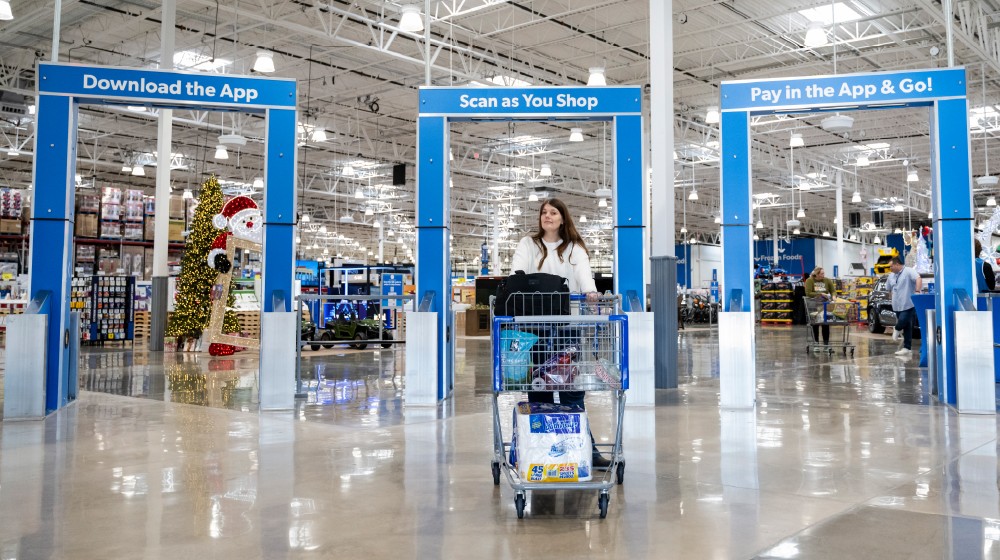 A woman pushing a shopping cart full of groceries out of a Sam's Club store.