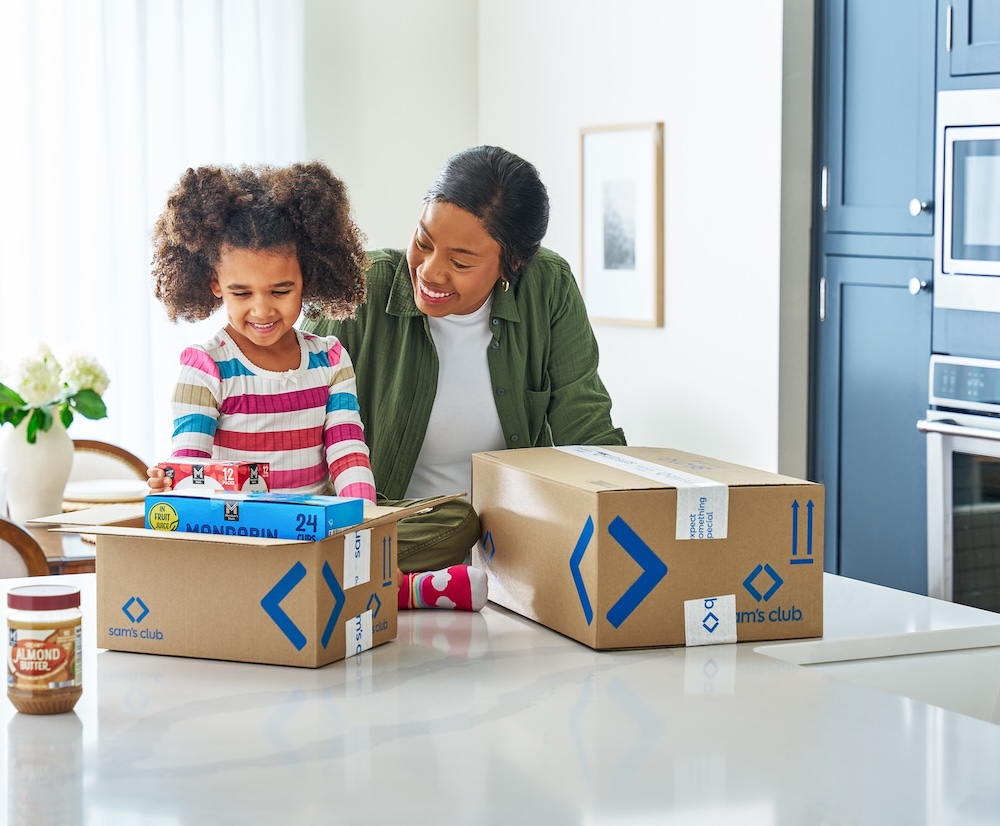 A smiling woman and a young girl open Sam's Club boxes together.