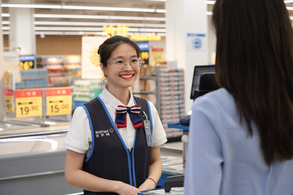 Walmart China associate wearing a blue vest and name tag smiles at a customer.