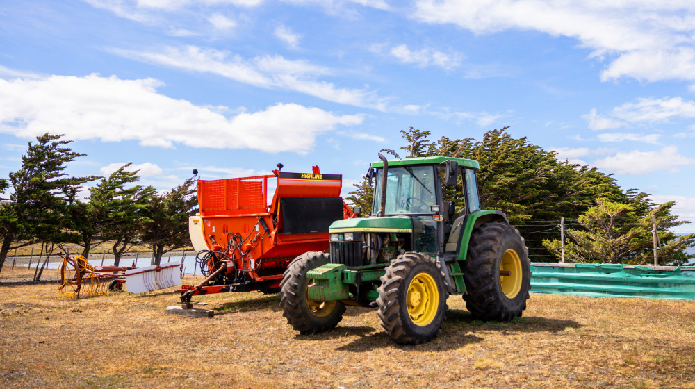 A green tractor next to a piece of red farm equipment in a field.