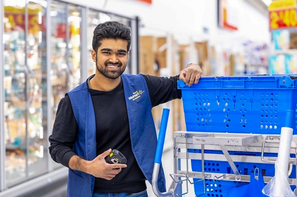 A smiling Walmart associate stands next to a large cart. 