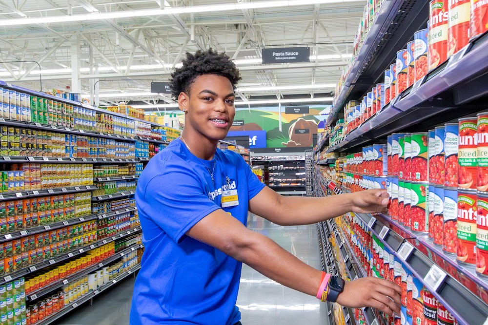 Walmart associate Deavontae stands next to canned tomatoes.