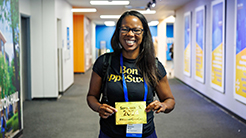 An Open Call participant is seen holding a yellow paper in a brightly lit Walmart office hallway. The setting features posters on the walls and a modern indoor environment.
