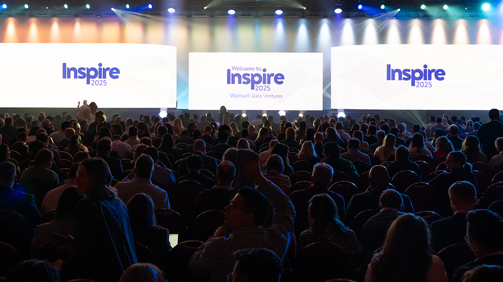 A large audience is seated in a dimly lit auditorium, facing three illuminated screens displaying 'Inspire 2025' and 'Welcome to Inspire 2025 Walmart Data Ventures'. 