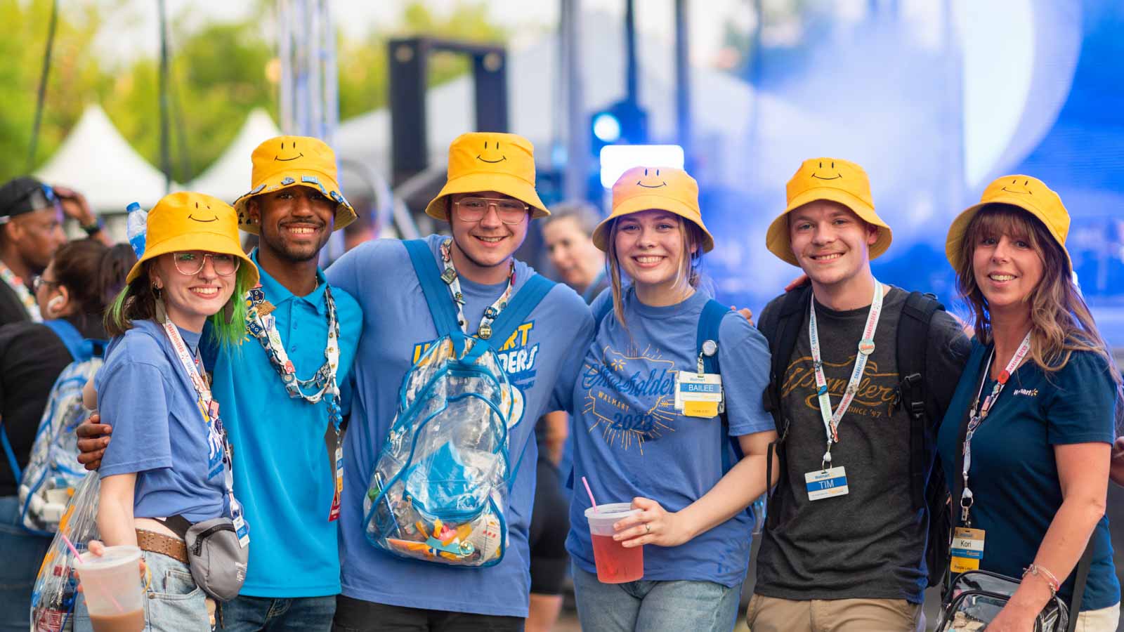 A group of Walmart associates stand for a picture, all wearing yellow smiley-face bucket hats.