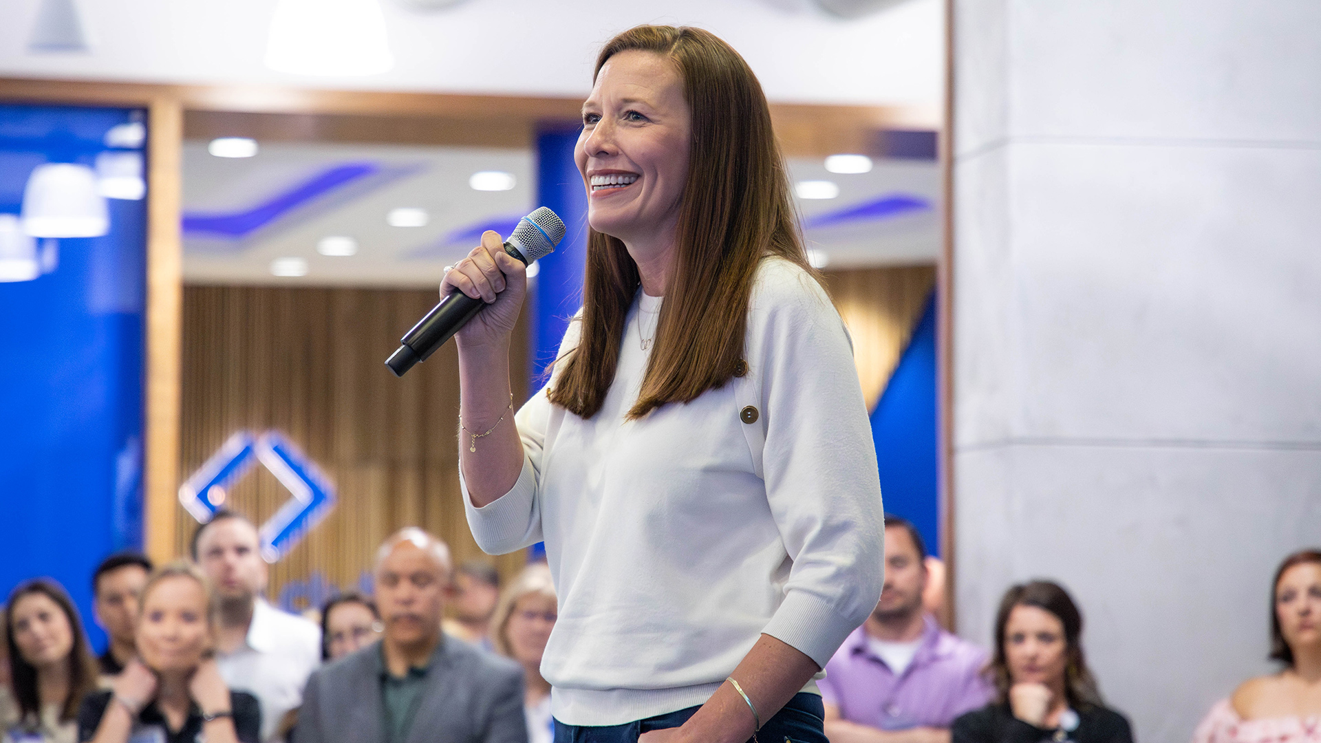 A woman holds a microphone and addresses a crowd.