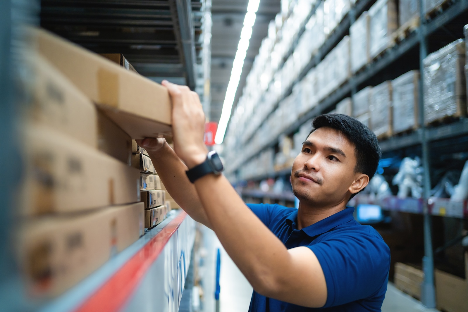 Worker in blue uniform loading boxes on a shelf at a distribution center. supply chain