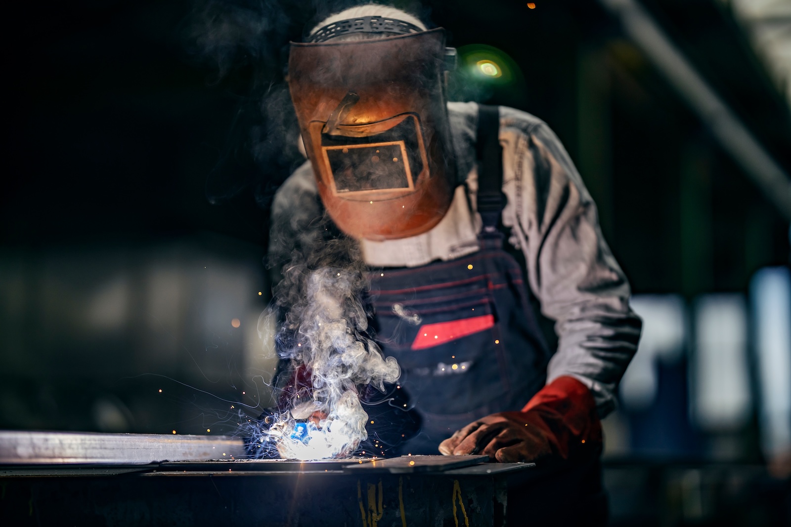 A metallurgy blue collar worker is welding metal parts at heavy industry plant.